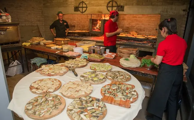 Equipo de La Vieja con remeras rojas preparando pizzas junto al horno